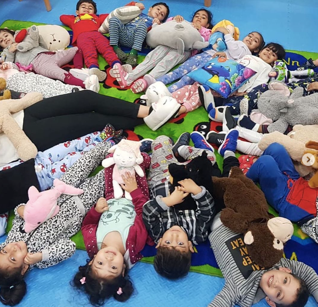 School children wearing pajamas laying in a circle with all of their feet in the middle 