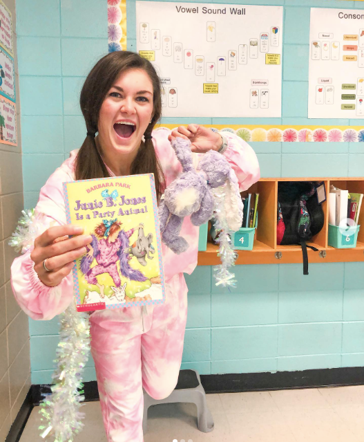 A teacher in her pajamas holds a Junie B Jones book and a stuffed animal as an example of pajama day ideas and activities