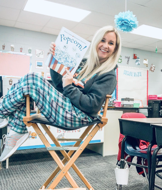 A teacher in jammies sits sideways in a directors chair holding up a children's book as an example of pajama day ideas and activities