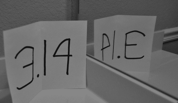 A sheet of paper with 3.14 is held up to a mirror as an example of pi day activities