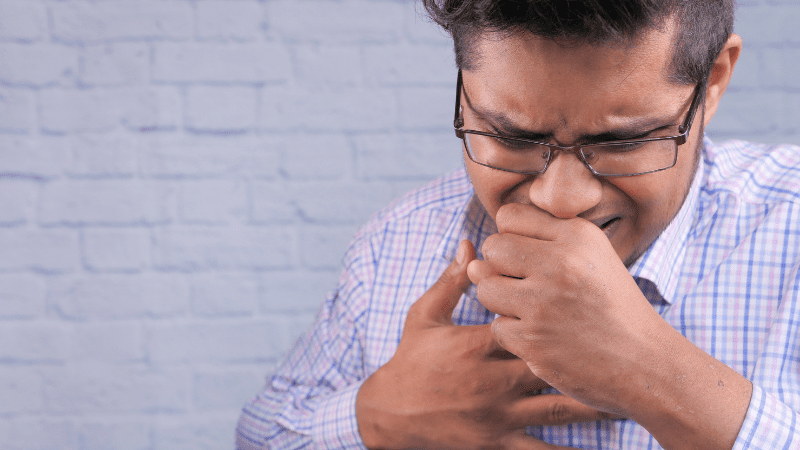 Young man in button down business shirt coughing into his hand