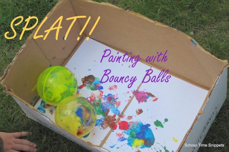 Two large green bouncy balls are shown dropping into a cardboard box that has paper and paint inside it.