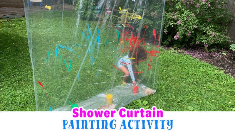 A child stands behind a clear shower curtain hanging up outside painting it in this collaborative art project.