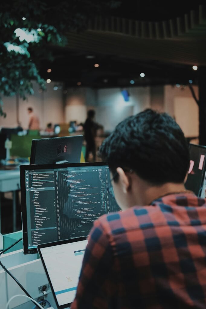 A software engineer sits with their back to a computer, typing code on a keyboard