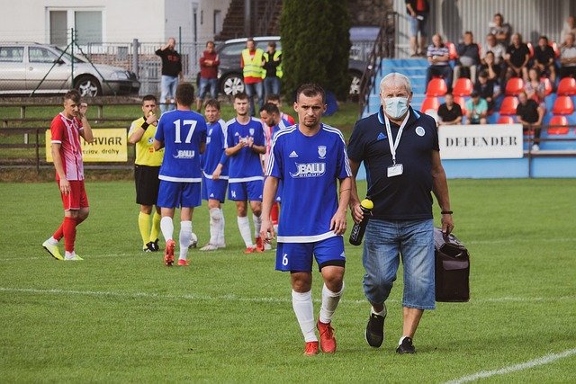 An athletic trainer helps an injured player off a football pitch
