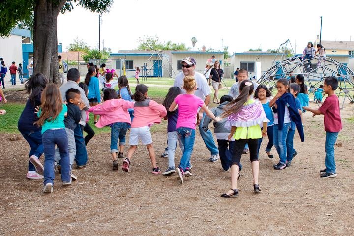 A large group of elementary school aged children are holding hands and running outside as an example of elementary PE games