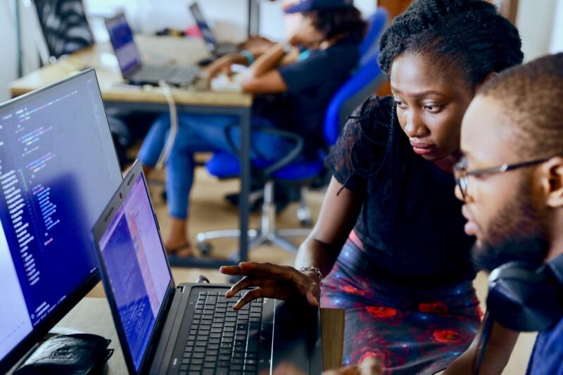 A computer research scientist looks at a set of laptop screens as another worker sits nearby