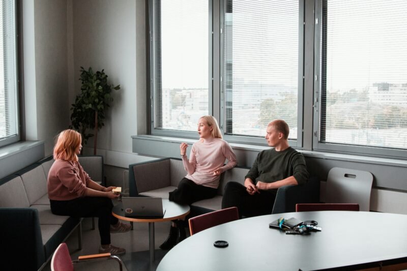 A mental health counselor speaks with two clients sitting on couches in an office with large windows
