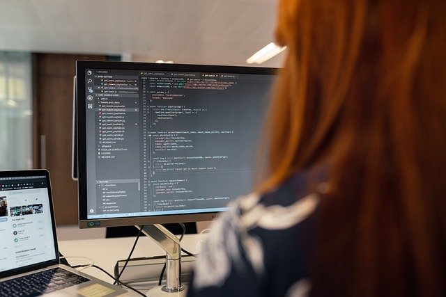 A software engineer sits with her back to a computer typing code on a keyboard
