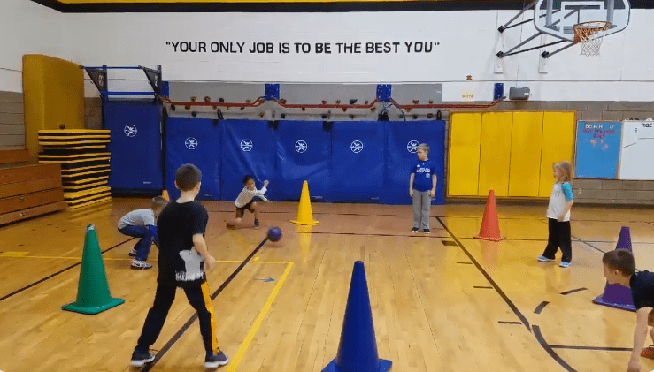 Large cones and students are spread around a gymnasium as an example of elementary PE games