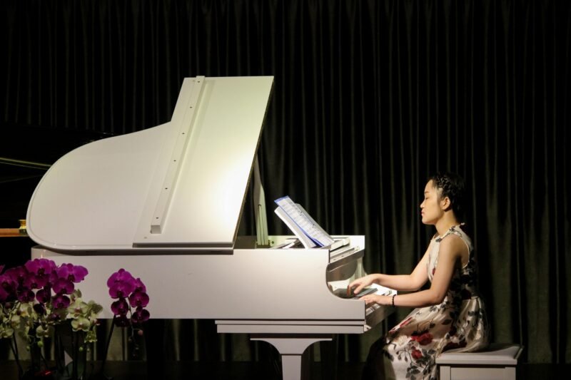 A woman sits at a white grand piano in this example of music careers.