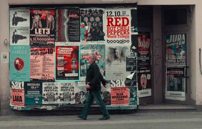 A man stands in front of a large wall covered in music concert posters.