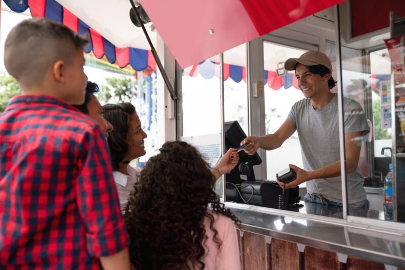Portrait of a happy family buying food at an amusement park and paying by card - lifestyle concepts