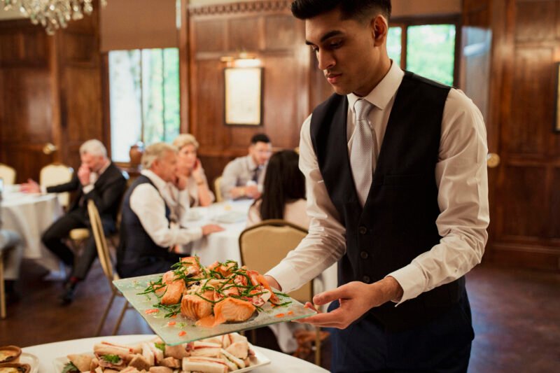 Waiter holding up a tray with salmon on it ready to setting up food on a buffet table at a business conference.