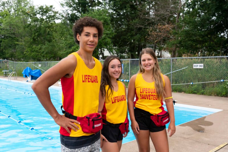 Three happy teenaged lifeguards on duty at an outdoor swimming pool.
