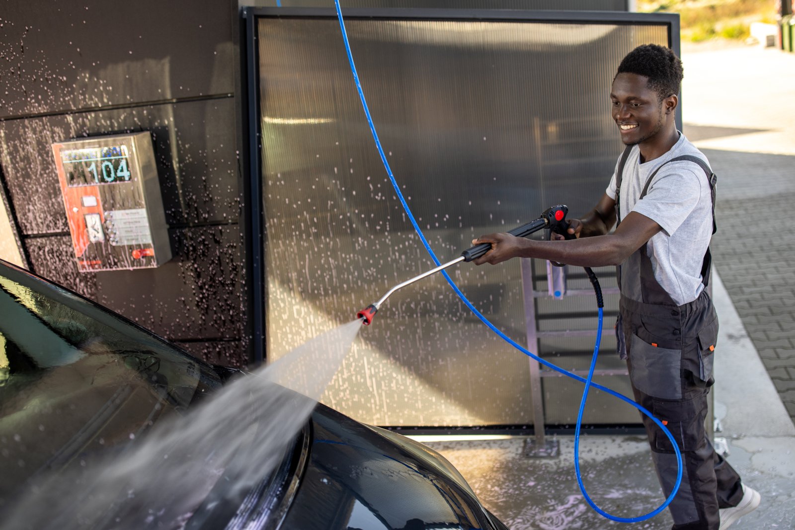 Skilled car wash professional sprays a car exterior with precision, using a water cannon.