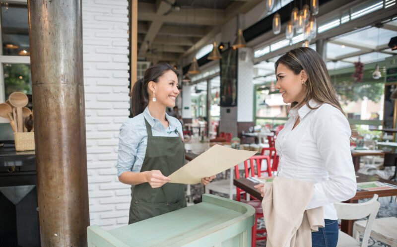 Friendly hostess working at a restaurant and talking to clients at the entrance