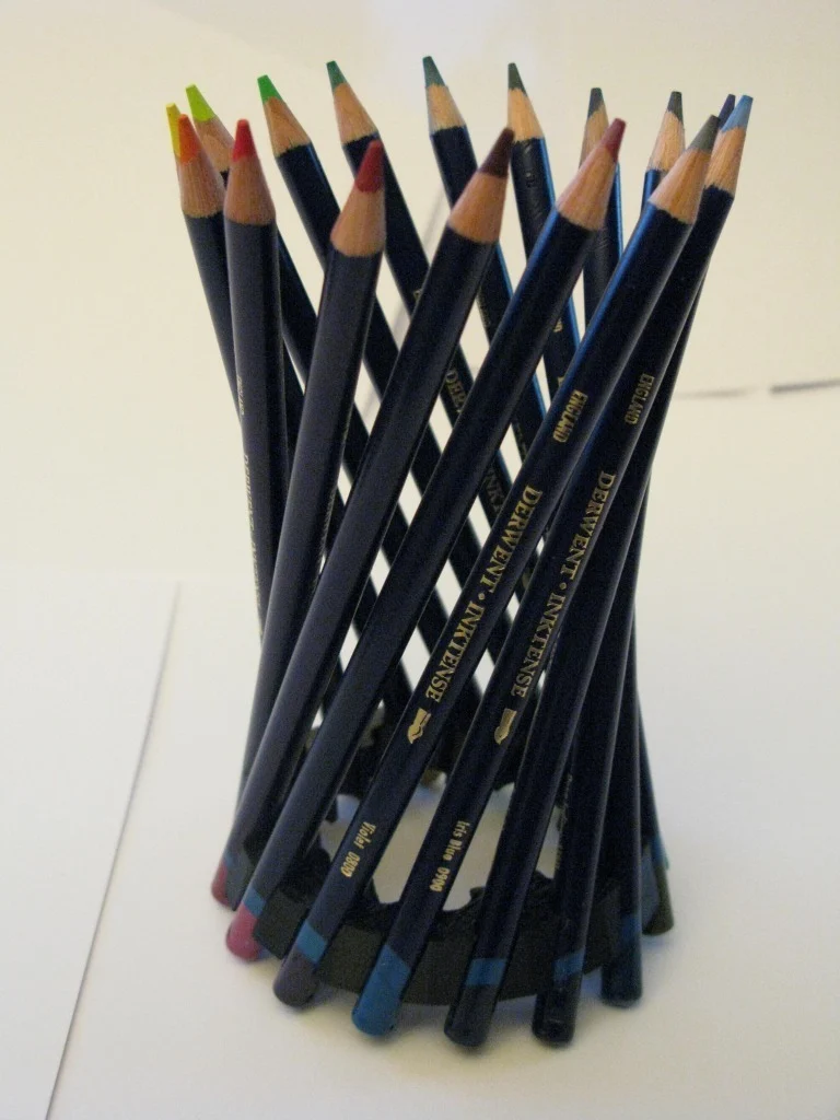 Several colored pencils are seen tilting in a circle in different directions. They are held together by a small circular holder at the bottom.