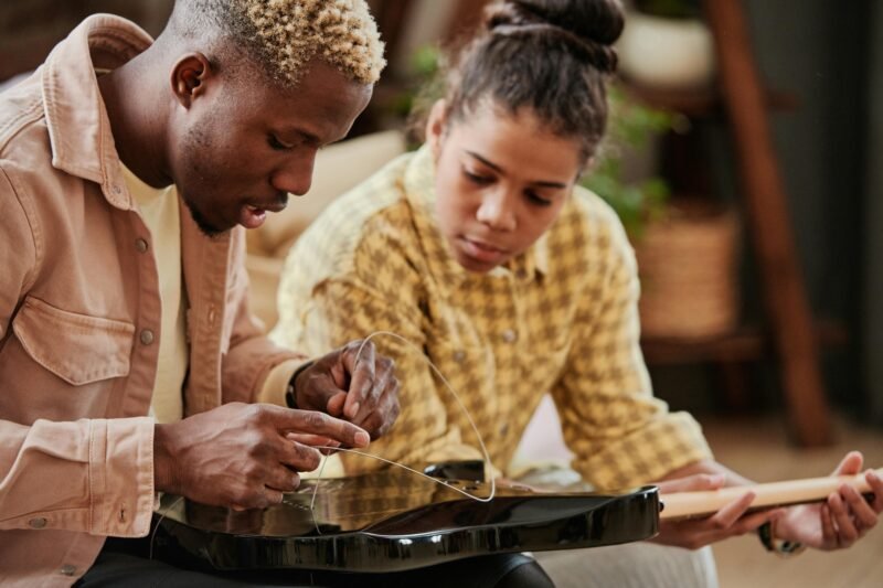 A man is seen re-stringing an instrument while a woman looks on.