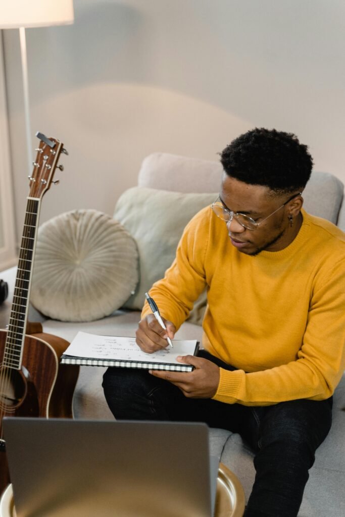 A man is seen writing on a notepad with a guitar in the background