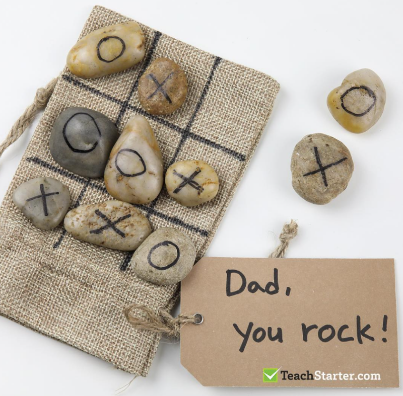 A burlap bag has rocks on top of it with Xs and Os drawn on them. The tag says, 