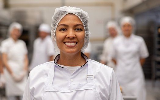Happy female employee working at a food factory and looking at the camera smiling