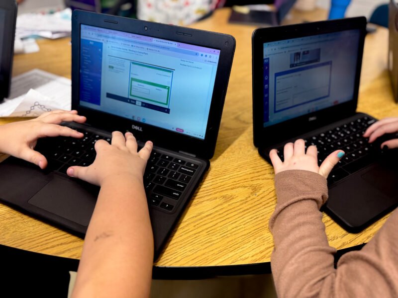 two kids hands typing on two laptops