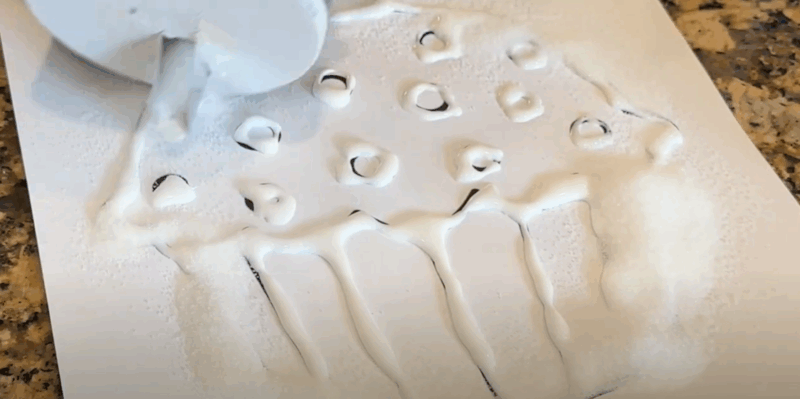 A cupcake coloring page that has glue drawn along the lines has salt painted over it. 