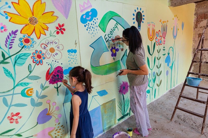 Child and teacher painting a mural in a school hallway
