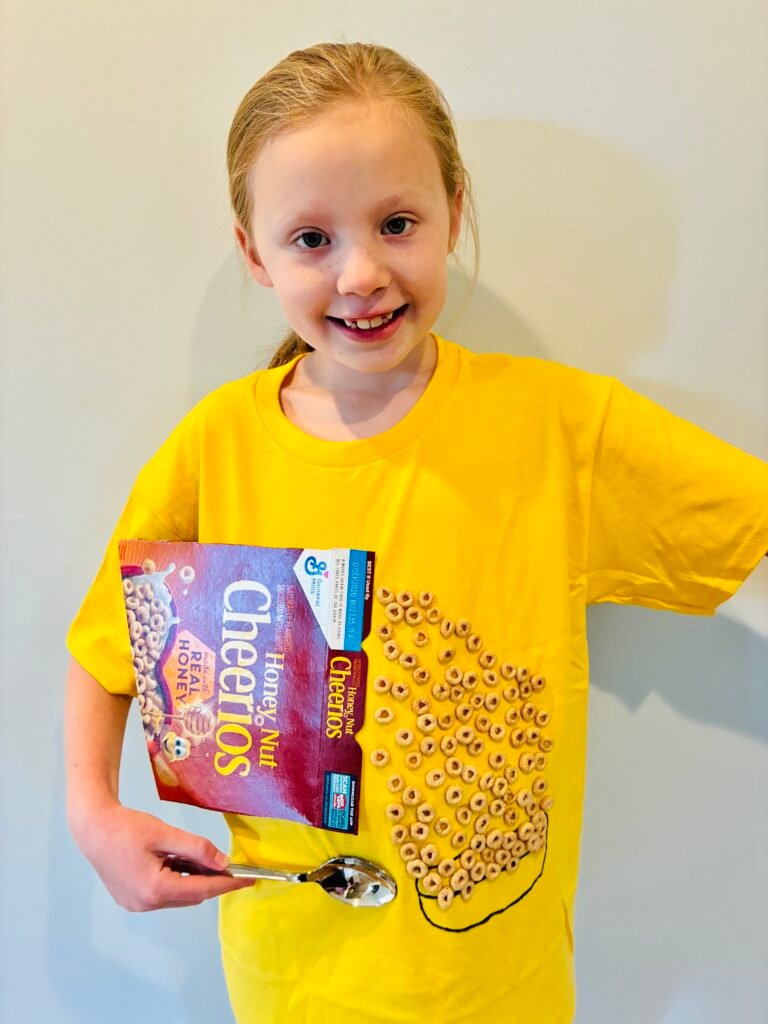 a student wearing a yellow shirt with a box of cheerios and a spoon with 100 cheerios to celebrate 100 days of school