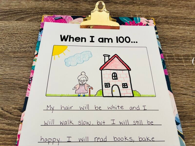 a floral clipboard holding a paper with the writing prompt: When I am 100... and a student response and drawing of themselves at 100