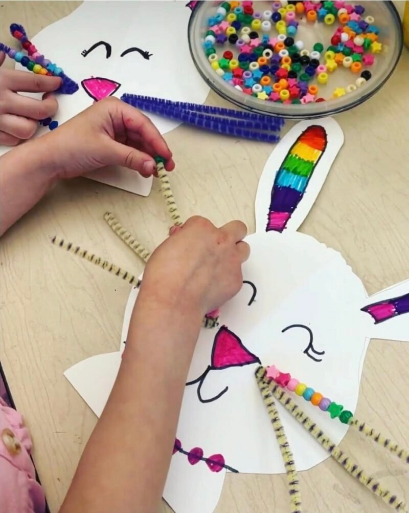 Child stringing beads onto a paper bunny's pipe cleaner whiskers