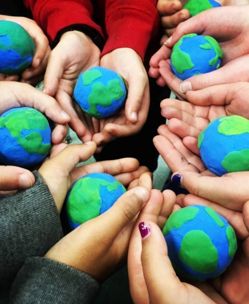 Children's hands holding models of the planet Earth made from clay pressed onto styrofoam balls