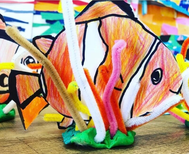 Paper fish sitting on a base of playdough with pipe cleaners to represent coral