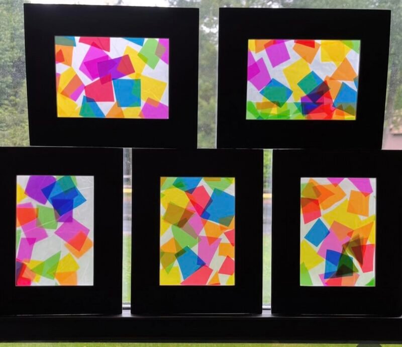 Black construction paper frames with tissue paper art displayed in a window