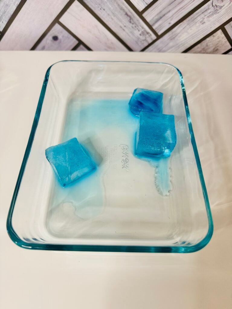 an image of three blue ice cube melting in a glass tray