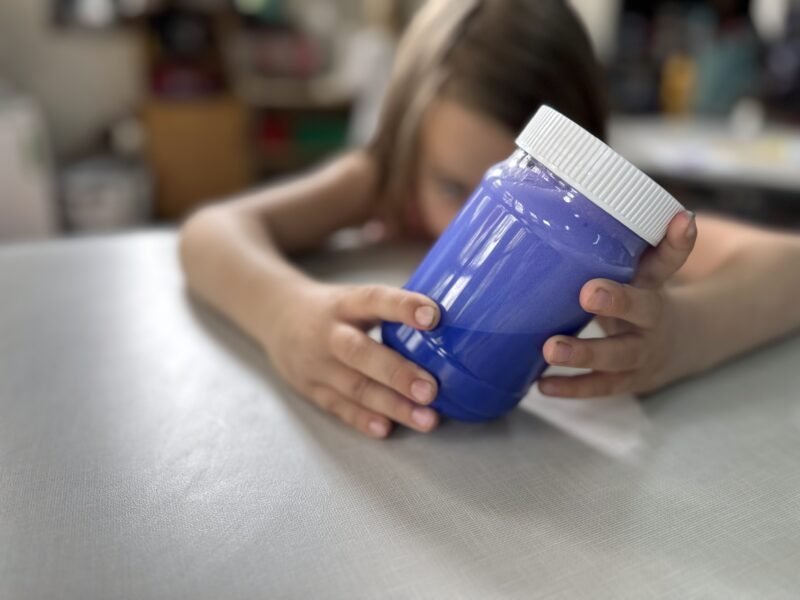 Calm Down Jar Girl sitting at desk in classroom holding a DIY calm down jar.